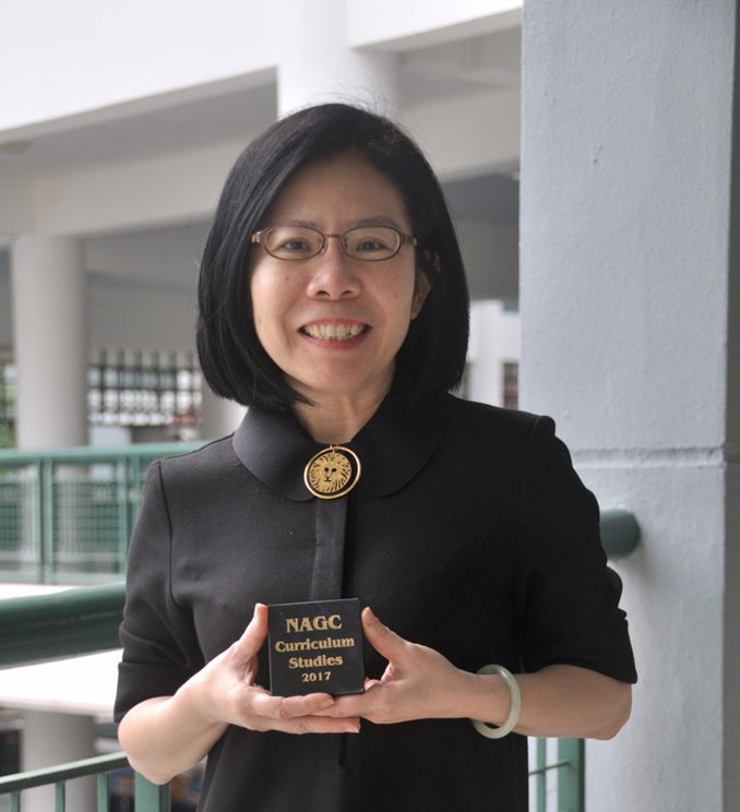 Woman in black jacket holding a small award reading NAGC Curriculum Studies 2017, smiling indoors.