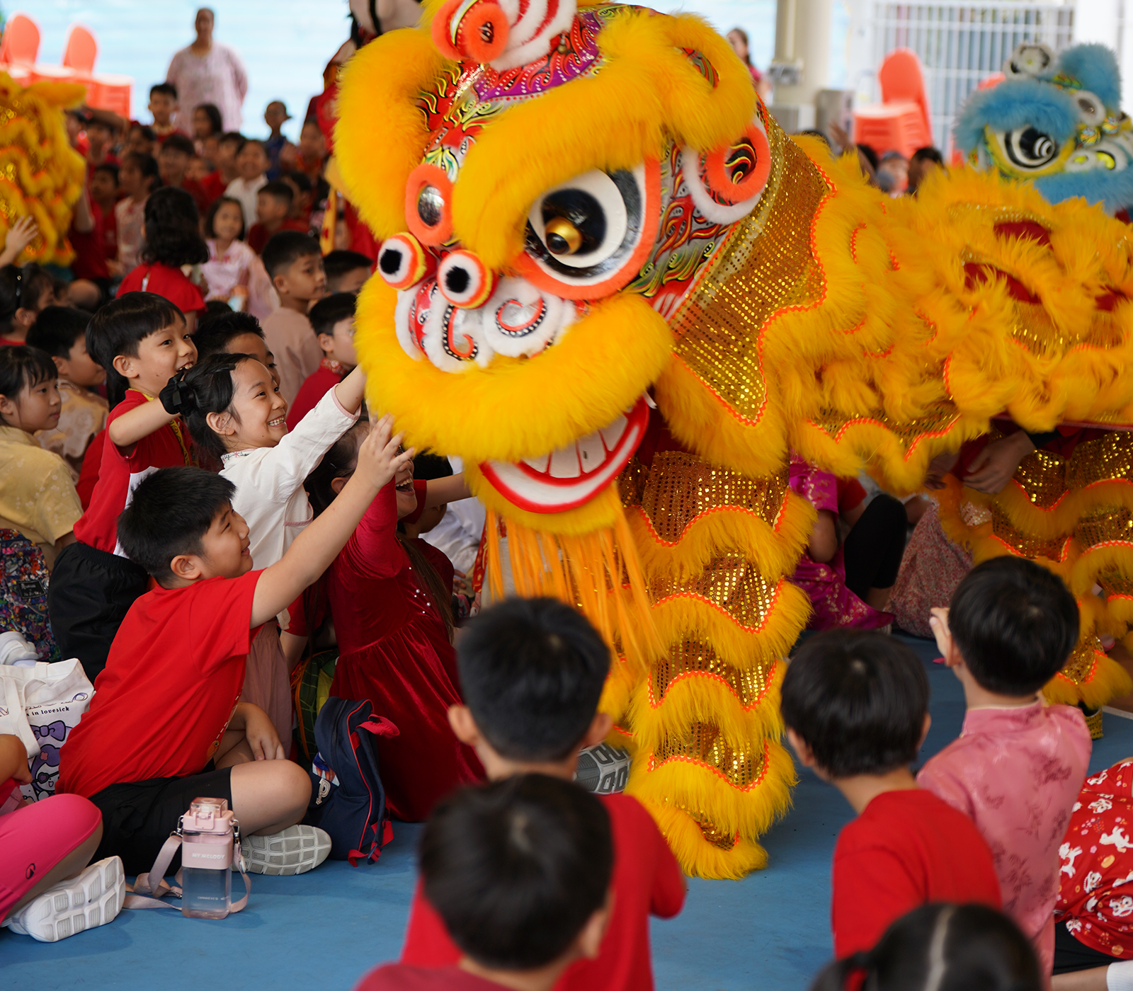 Children in red shirts reach out to touch a bright yellow Chinese lion dance costume during a festive performance.