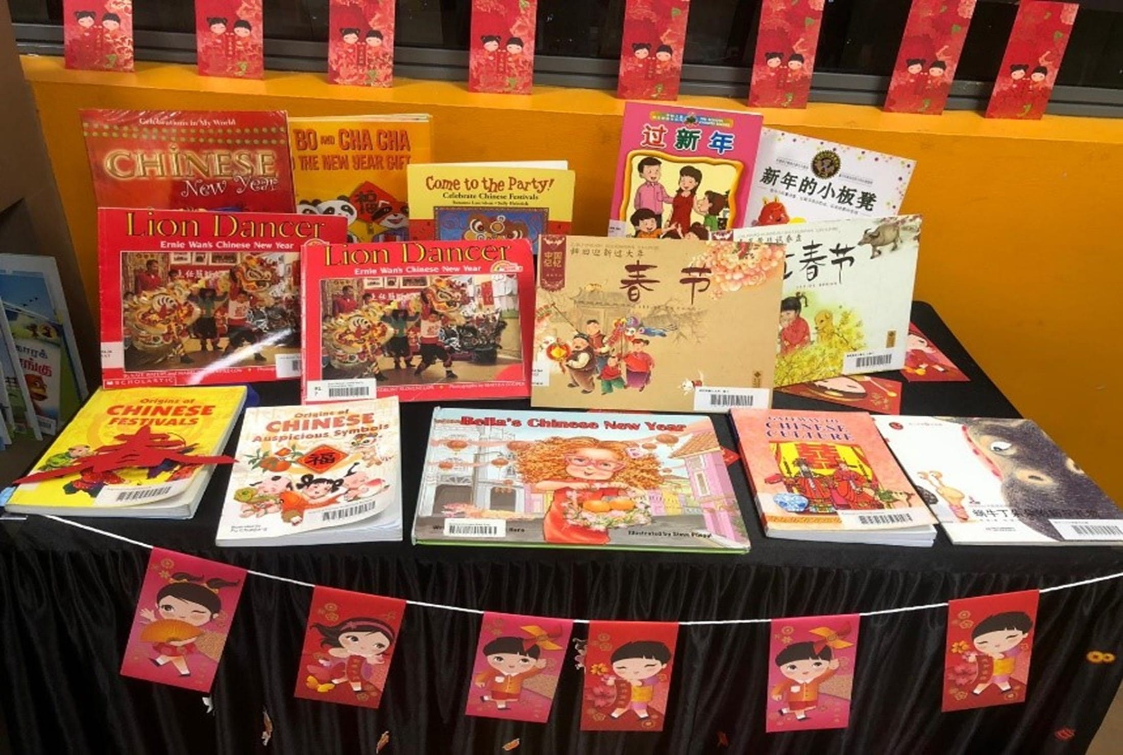 A table display of Chinese New Year children's books decorated with red festive banners and cartoon character cutouts.