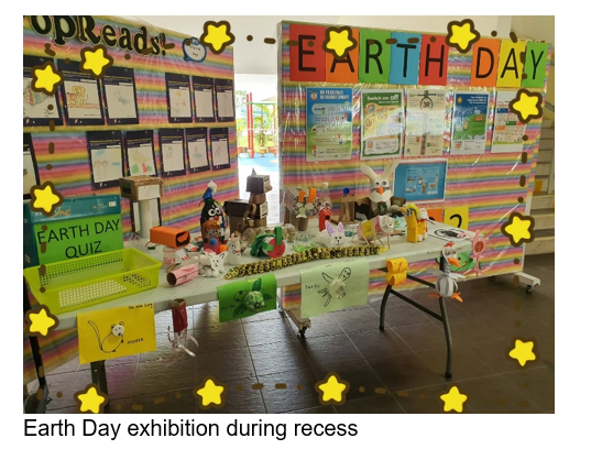 A school Earth Day display with colorful boards, crafts on a table, and an Earth Day Quiz sign, decorated with star stickers.