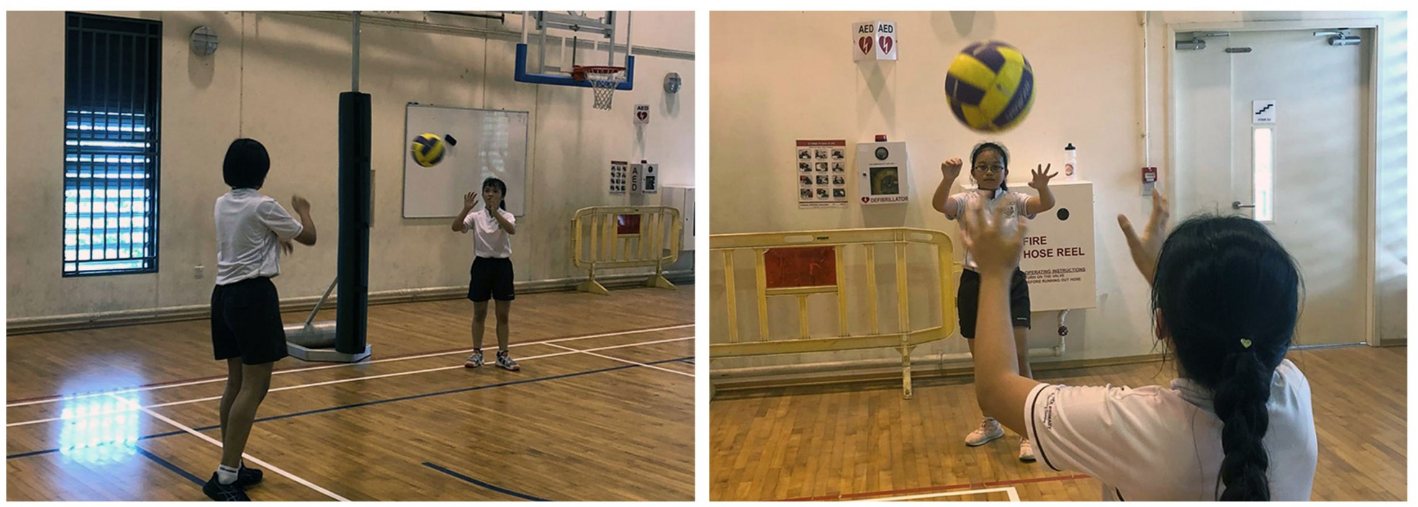 Two school girls in uniforms practice passing a volleyball to each other.