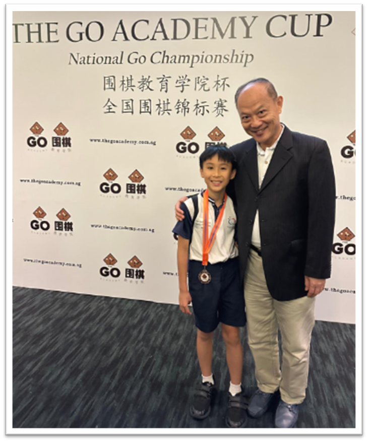 A young boy wearing a medal stands with an older man in front of a Go Academy Cup National Championship banner.