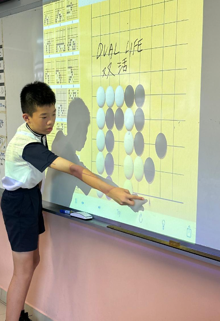 A boy points at a projected board game screen showing Go pieces and the text "Dual Life" with Chinese characters.