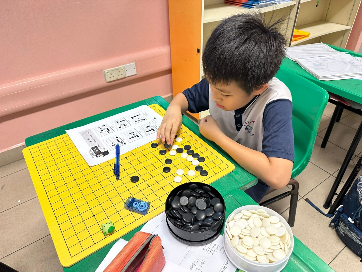 Young boy placing black stones on a yellow Go board, with bowls of black and white stones nearby.