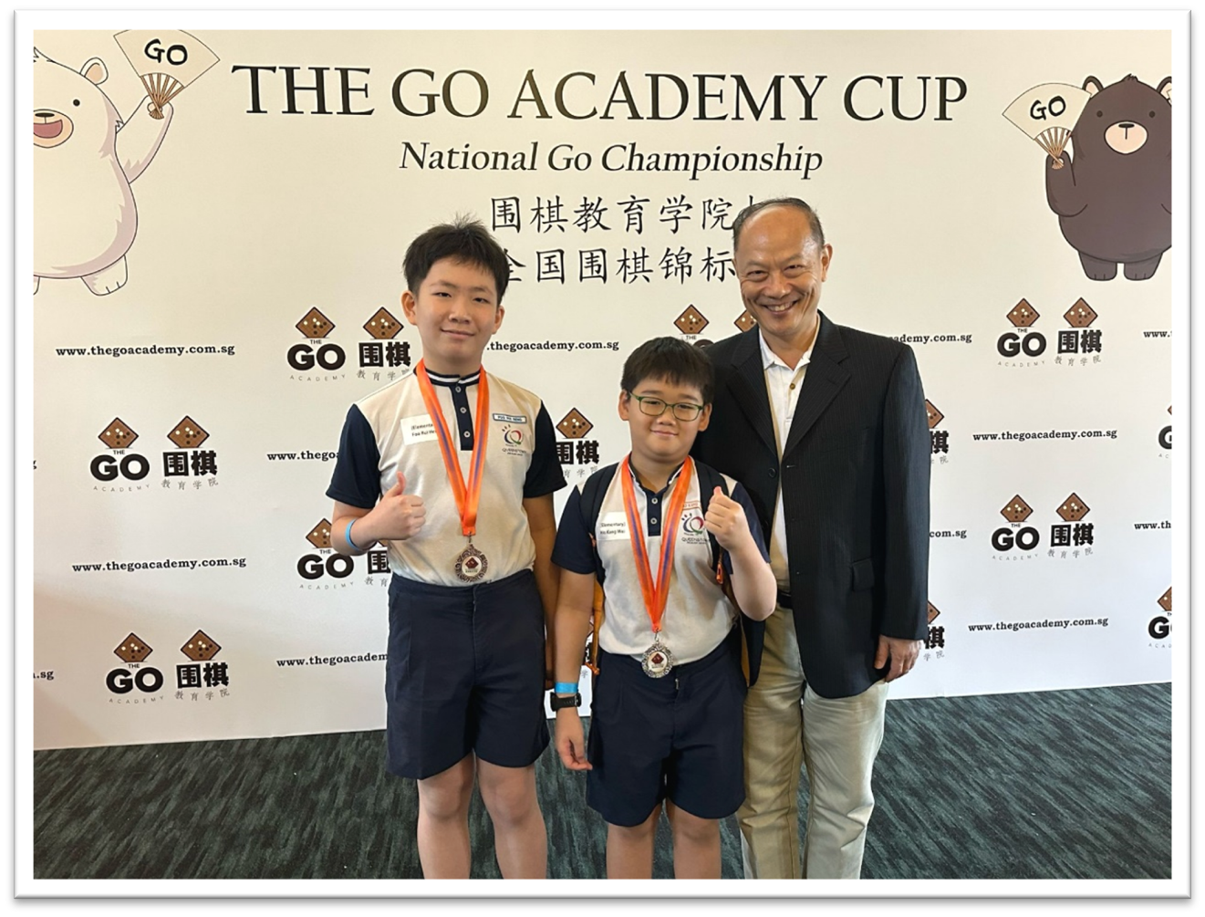 Two boys wearing medals and an older man pose in front of The Go Academy Cup National Go Championship banner.