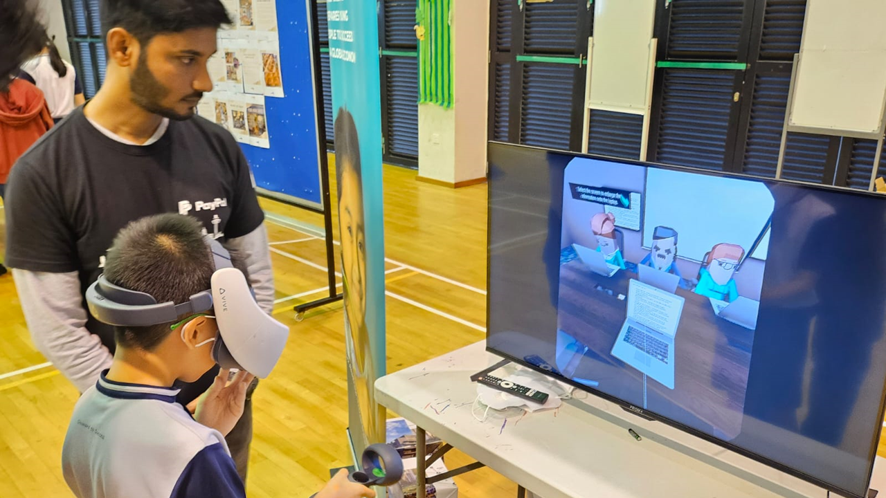 A child wearing a VR headset uses controllers while an adult watches, with a screen showing a cartoon scene nearby.