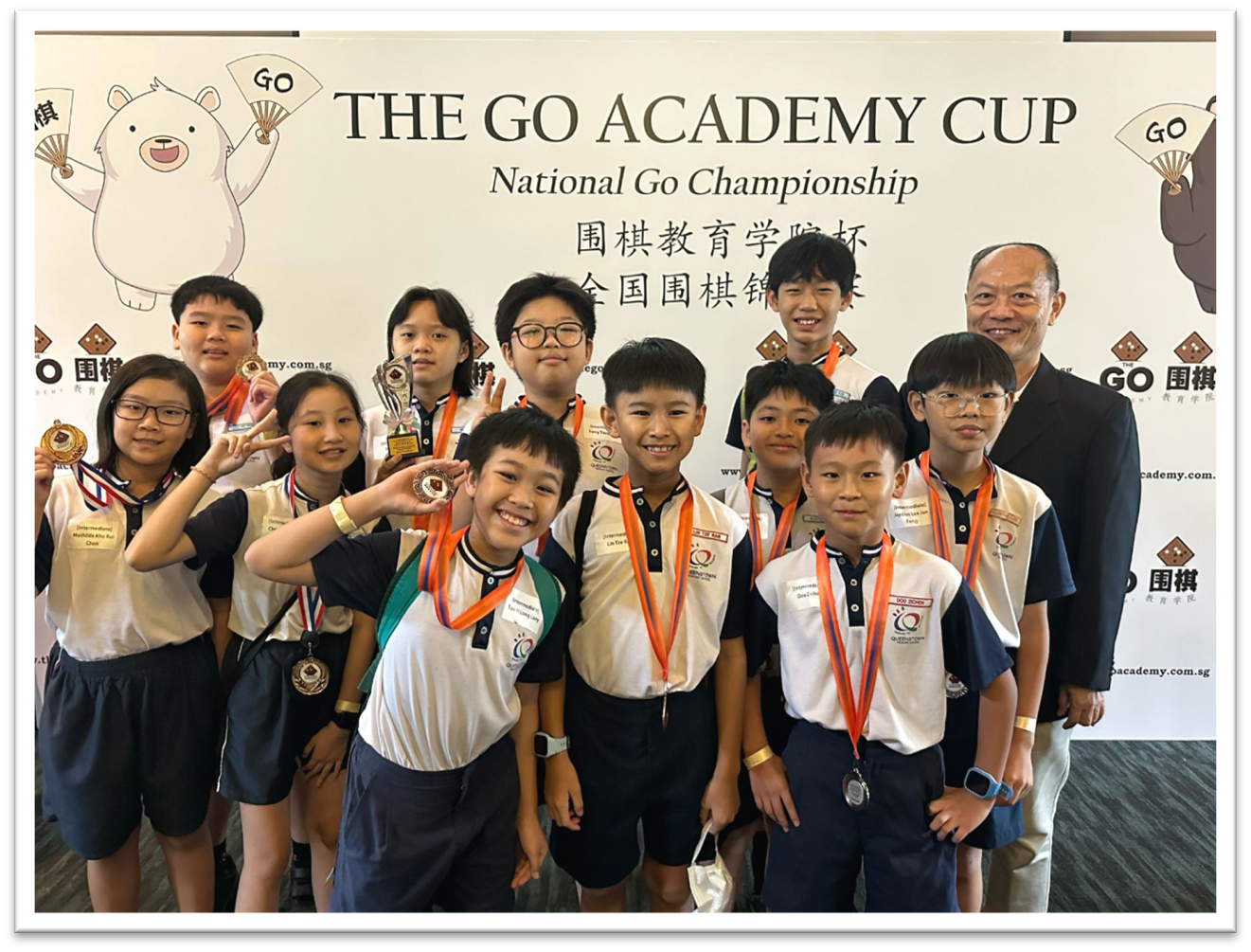 A group of children wearing medals pose with an adult in front of a Go Academy Cup National Go Championship banner.