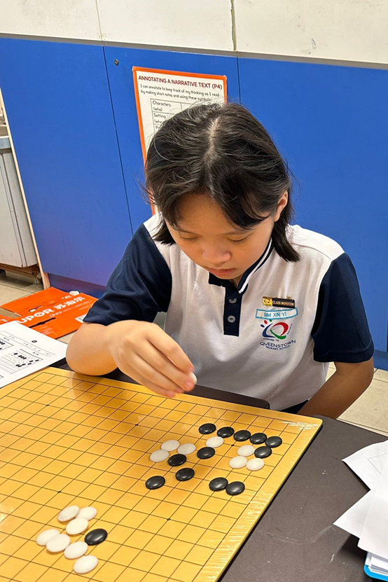 A young student in a school uniform placing a stone on a Go board with black and white pieces.