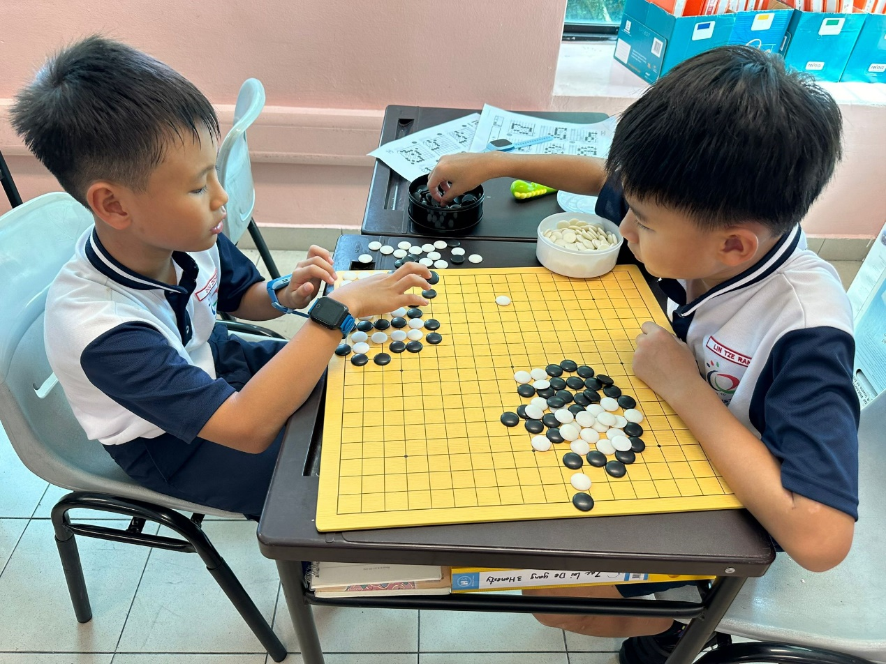 Two young boys in school uniforms playing a game of Go with black and white stones on a yellow board.