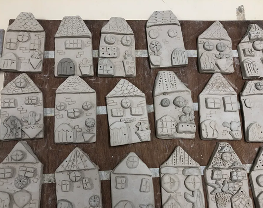 Multiple gray clay house tiles with textured details like windows and doors arranged on a brown wooden board.