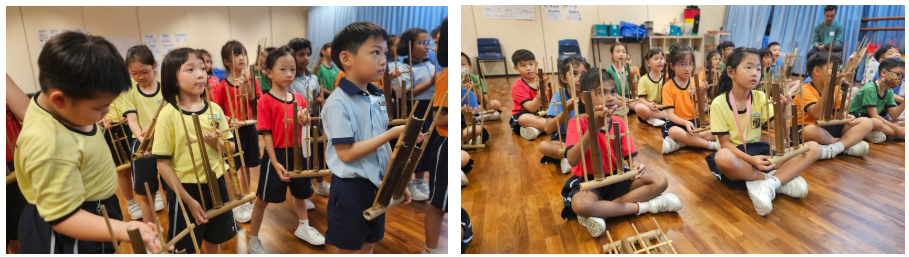 Children in yellow uniforms stand and sit on a wooden floor holding bamboo musical instruments indoors.