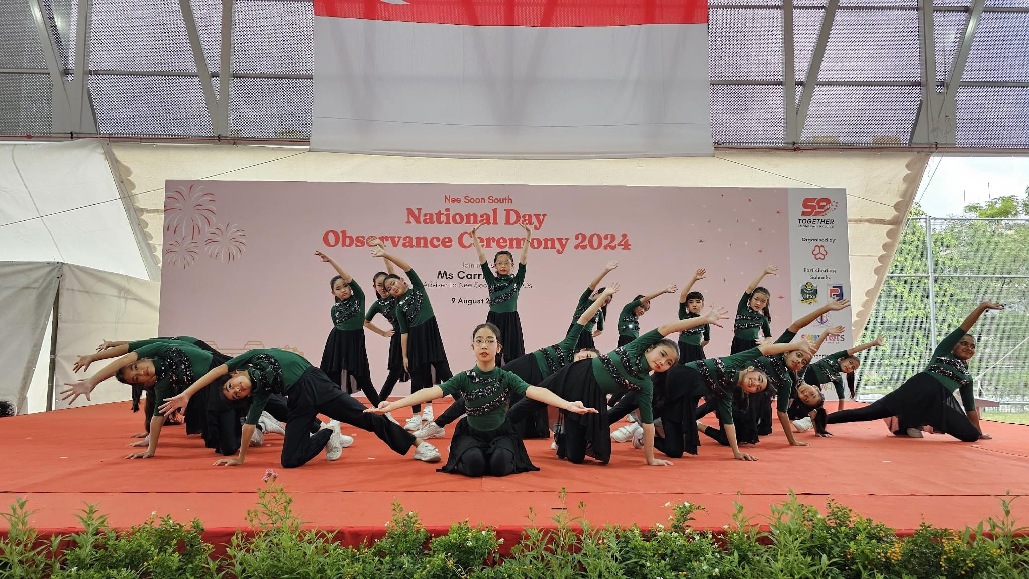 Students in green and black outfits perform a dance on a red stage at Nee Soon South National Day Observance Ceremony 2024.