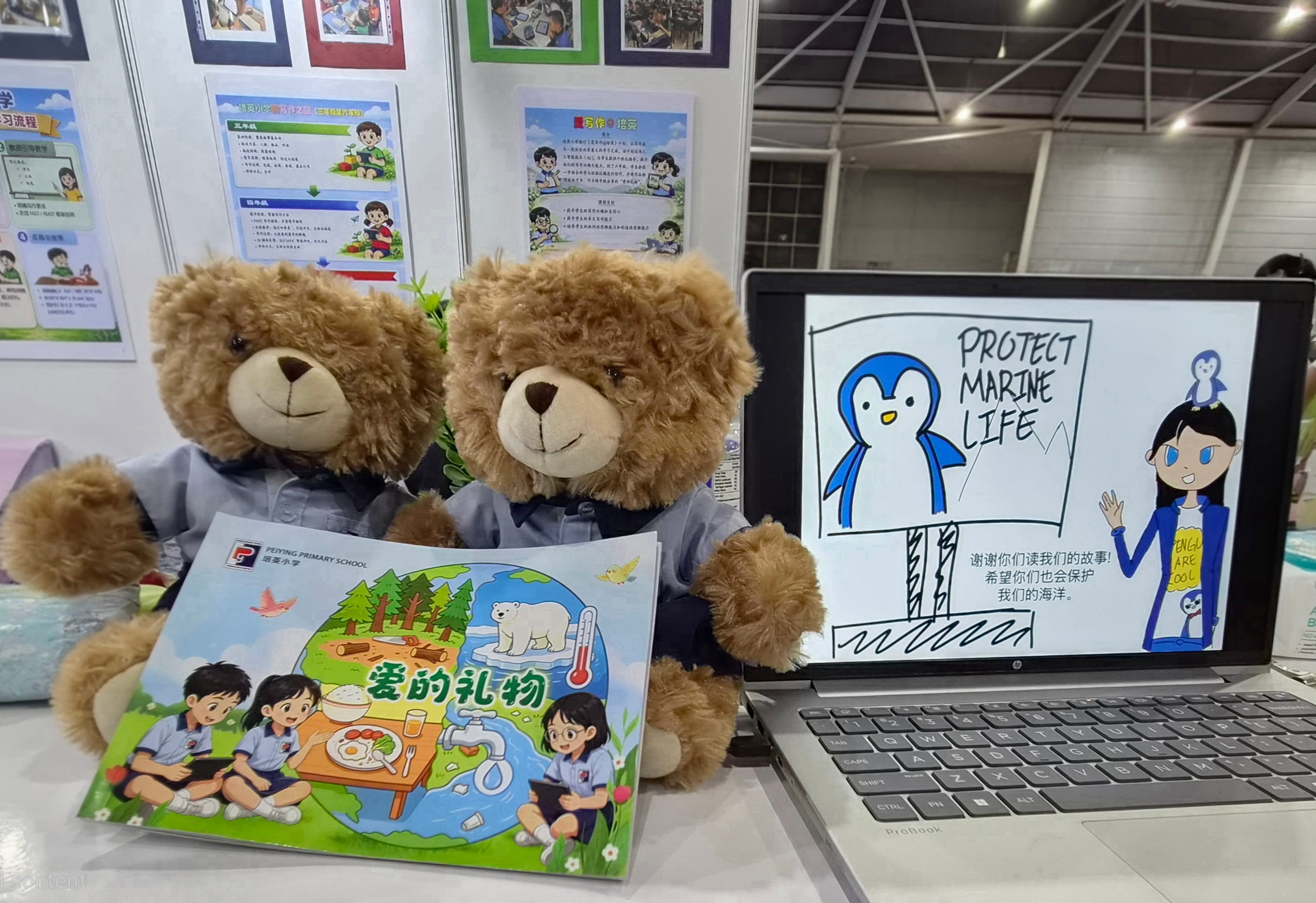 Two teddy bears sitting next to a picture book and a laptop displaying a penguin drawing.
