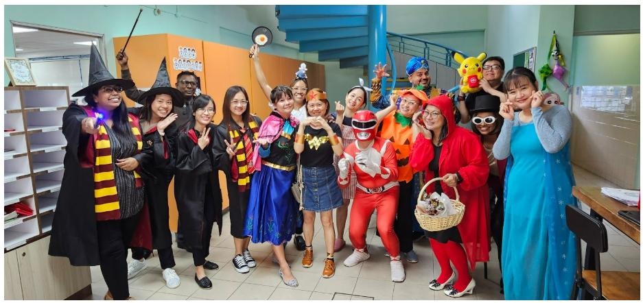 A large group of people posing in colorful Halloween costumes including witches, Power Ranger, pumpkin, and Pikachu.