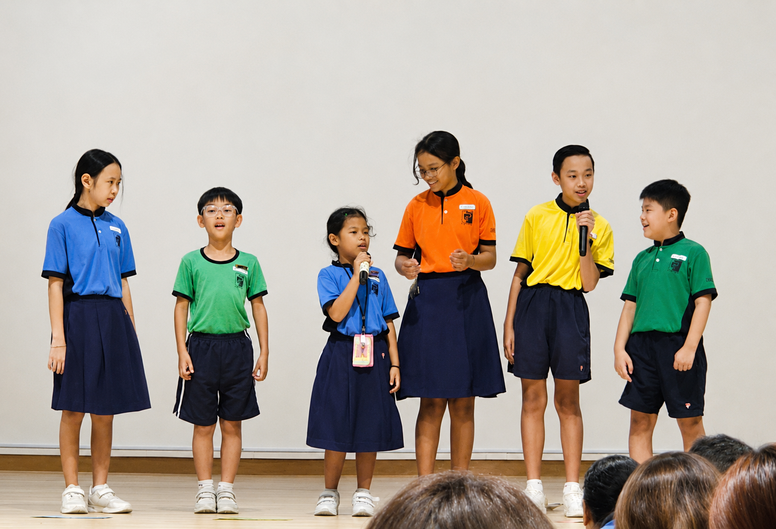 A group of students in colorful polo shirts standing on stage holding microphones.