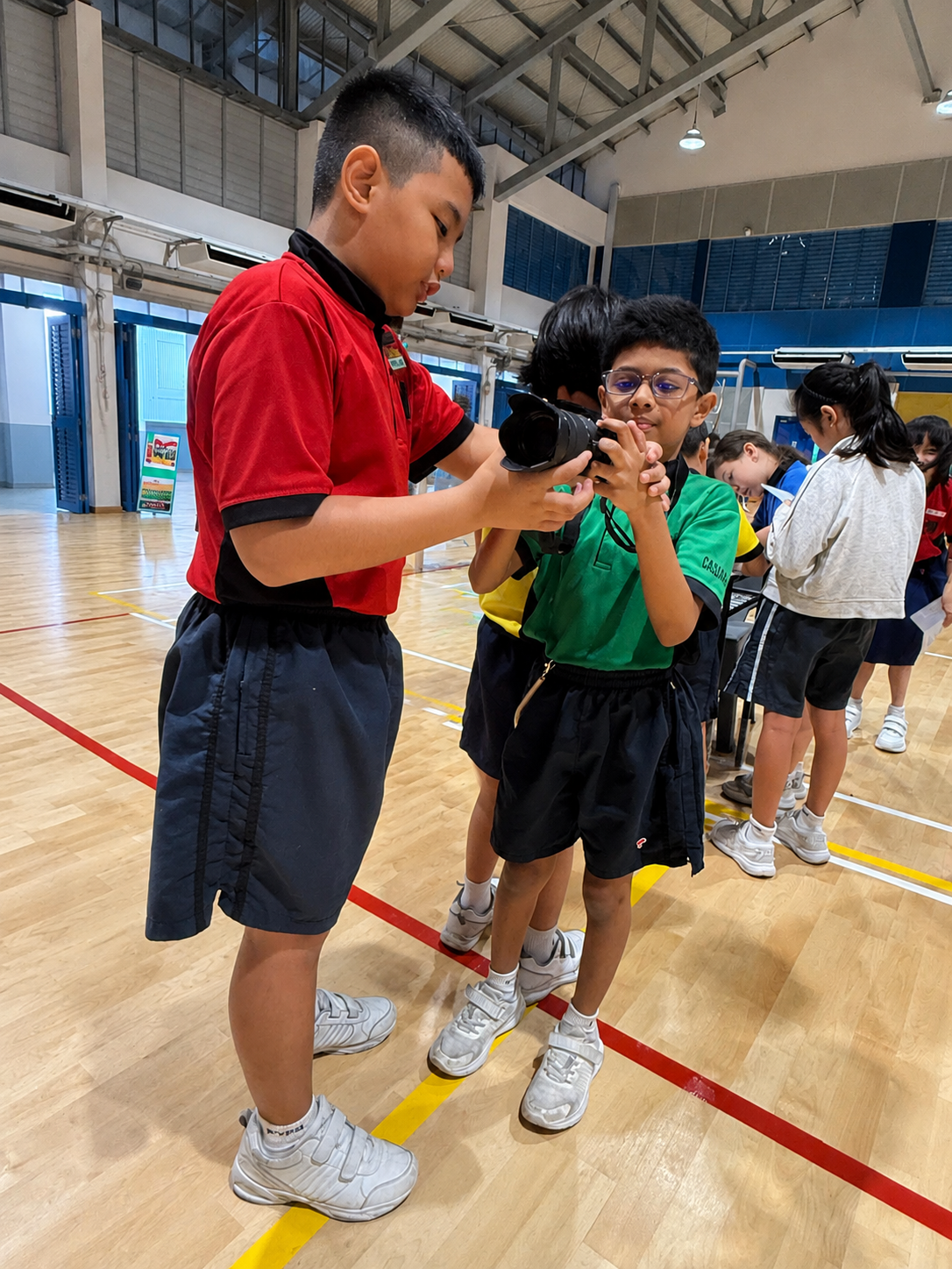 A student leader guiding Primary 2 students using a digital device during a school activity.