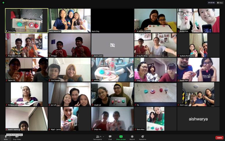 A video call with multiple participants, many holding small colorful clay crafts they made during an online workshop.