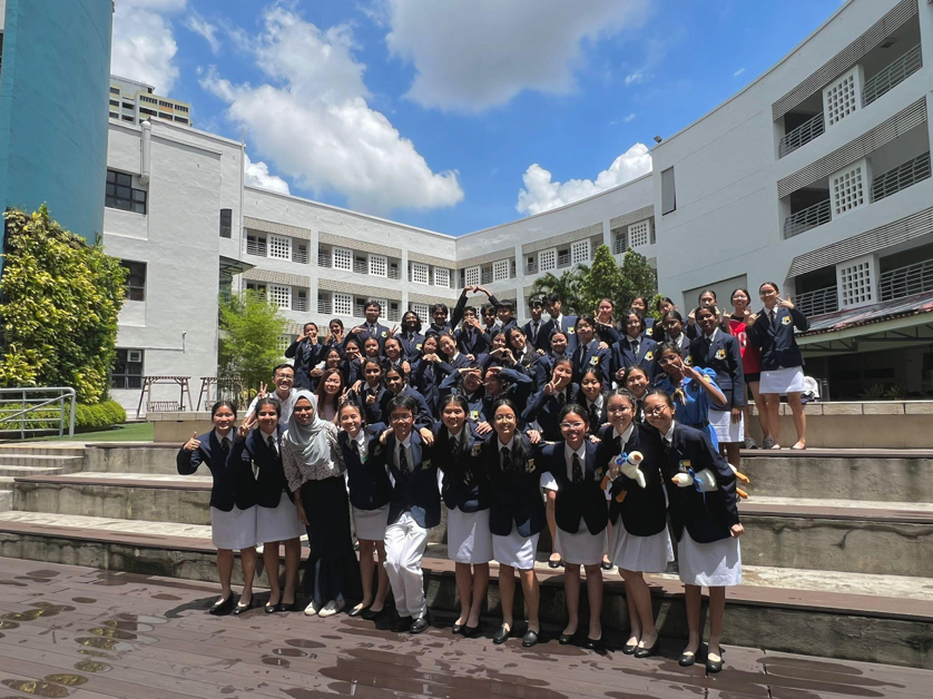 Large group of students in navy blazer uniforms posing on outdoor steps in front of a white school building.