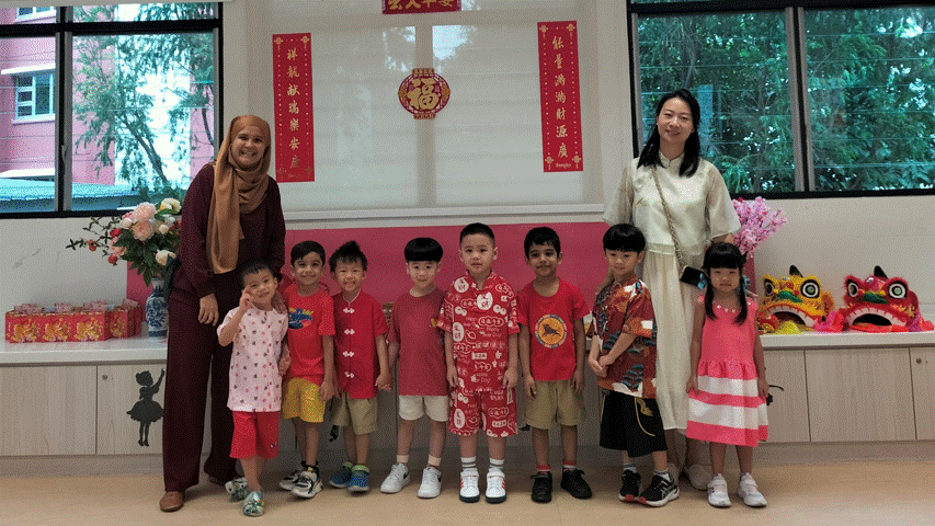 Two women and six young children pose indoors before Chinese New Year decorations including red banners and a lion head.