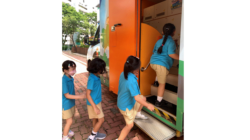 Four young girls in blue uniforms line up to board a colorful orange vehicle outdoors.