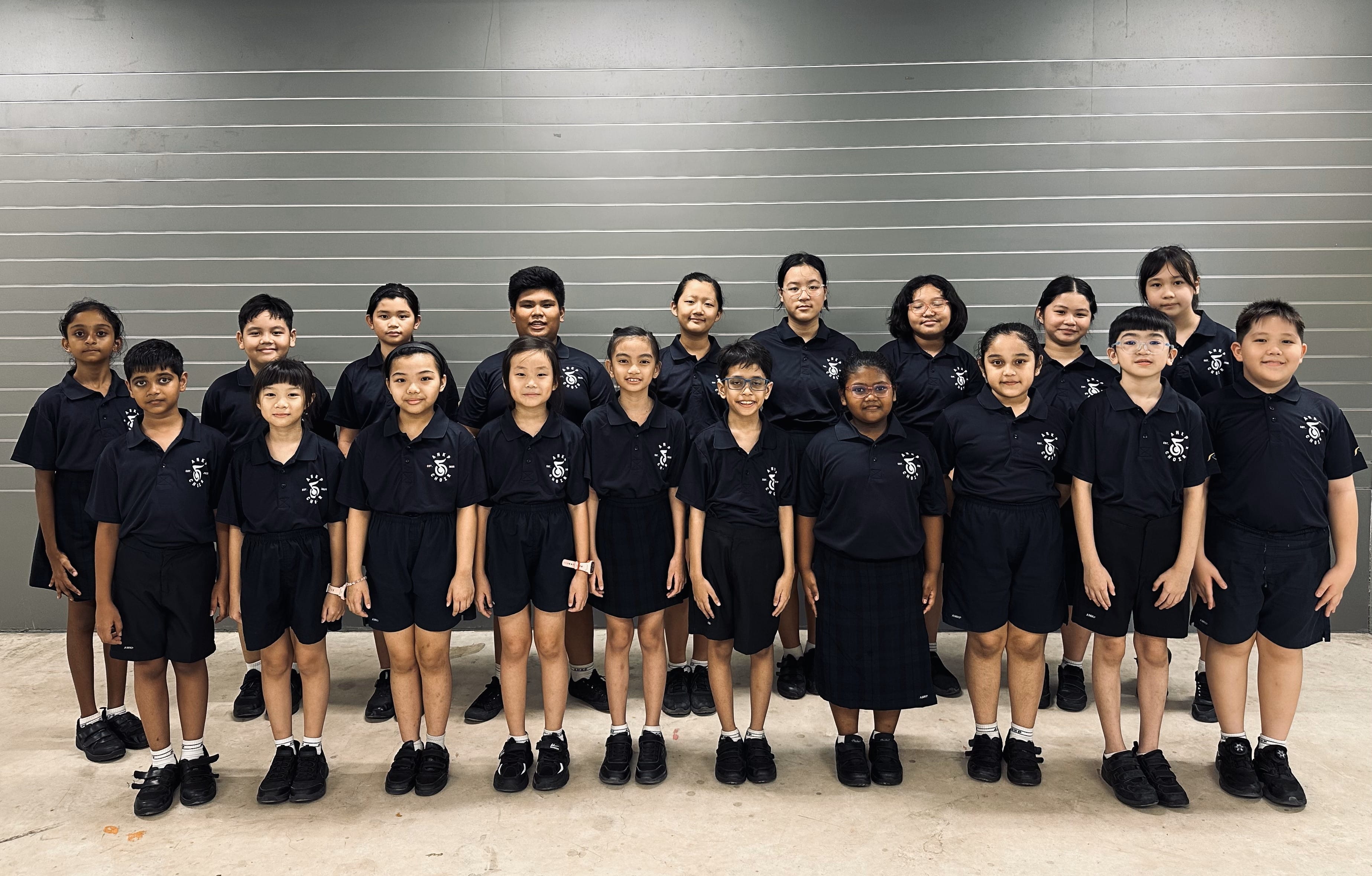 A group of about 20 children in matching dark navy school uniforms posing together in two rows indoors.