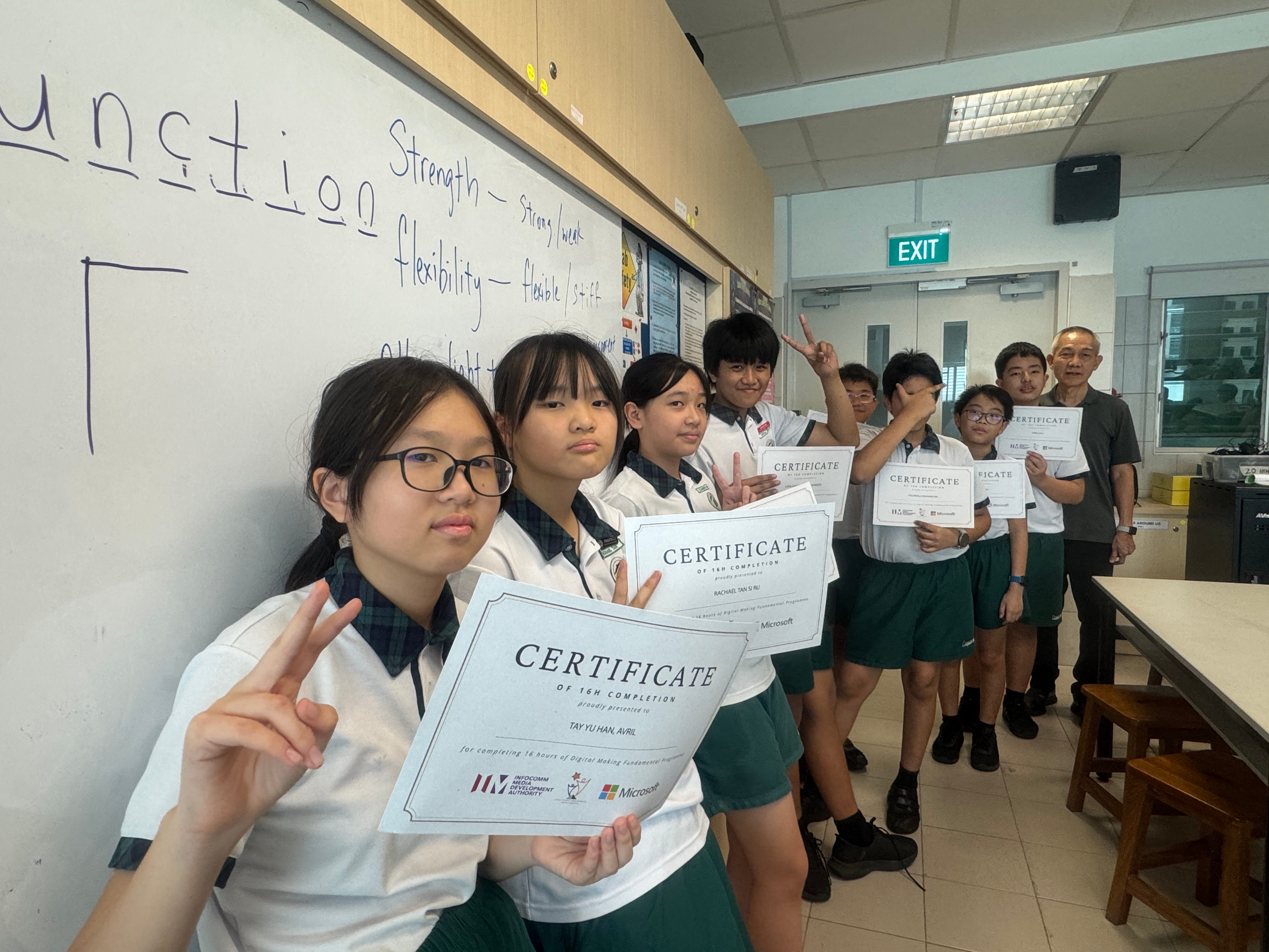 Students in school uniforms hold Microsoft completion certificates and make peace signs in a classroom.