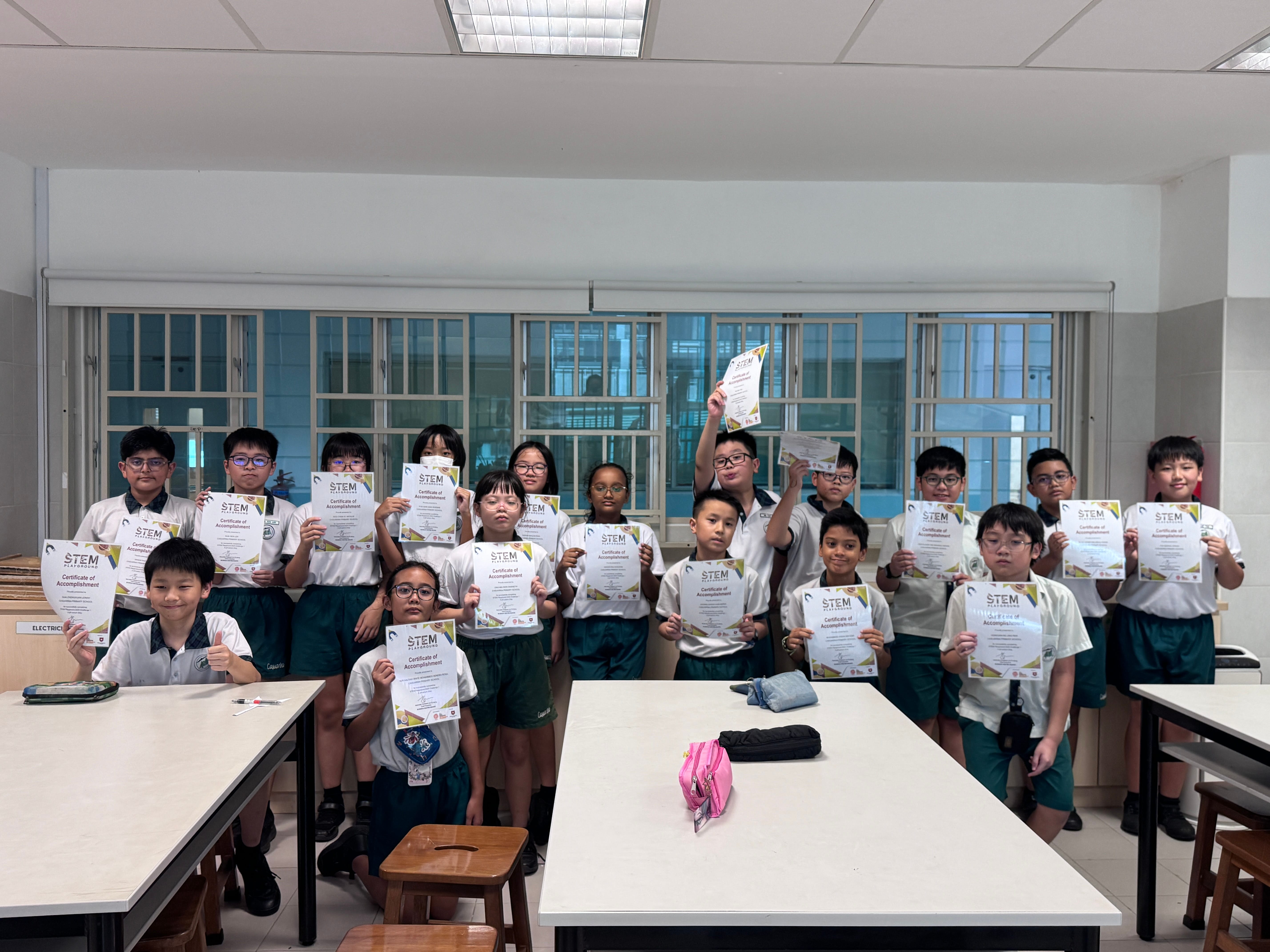 Group of young students in school uniforms holding up STEM Certificates of Accomplishment in a classroom.