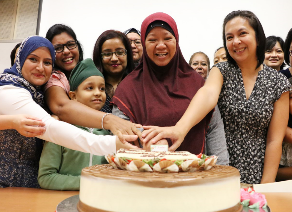 A group of smiling women and a child cut a decorated cake together at a celebration.