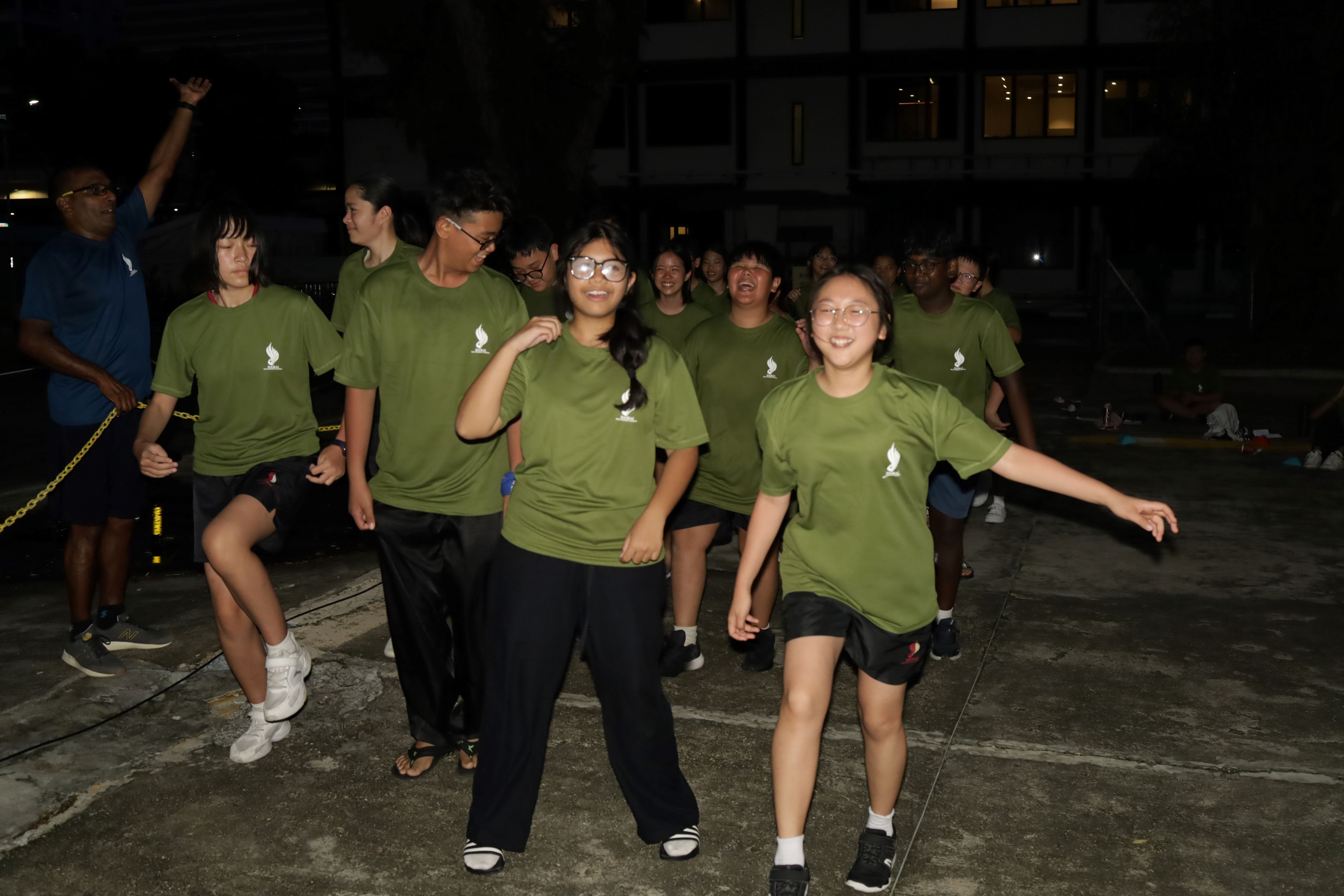 Group in matching green shirts walking and laughing outdoors at night, with buildings lit behind them