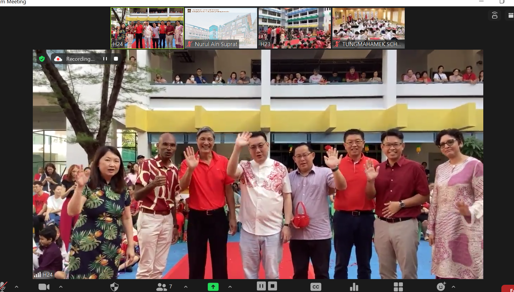 A Zoom meeting screen showing eight people waving at a school outdoor event, mostly wearing red outfits.