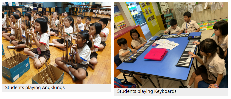 Young students sit on a floor playing angklungs, while other children play roll-up keyboards at a blue table.