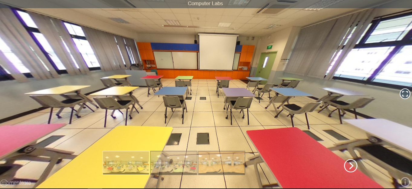 A 360-degree view of a computer lab with colorful desks, chairs, a projector screen, and orange cabinets at the front.