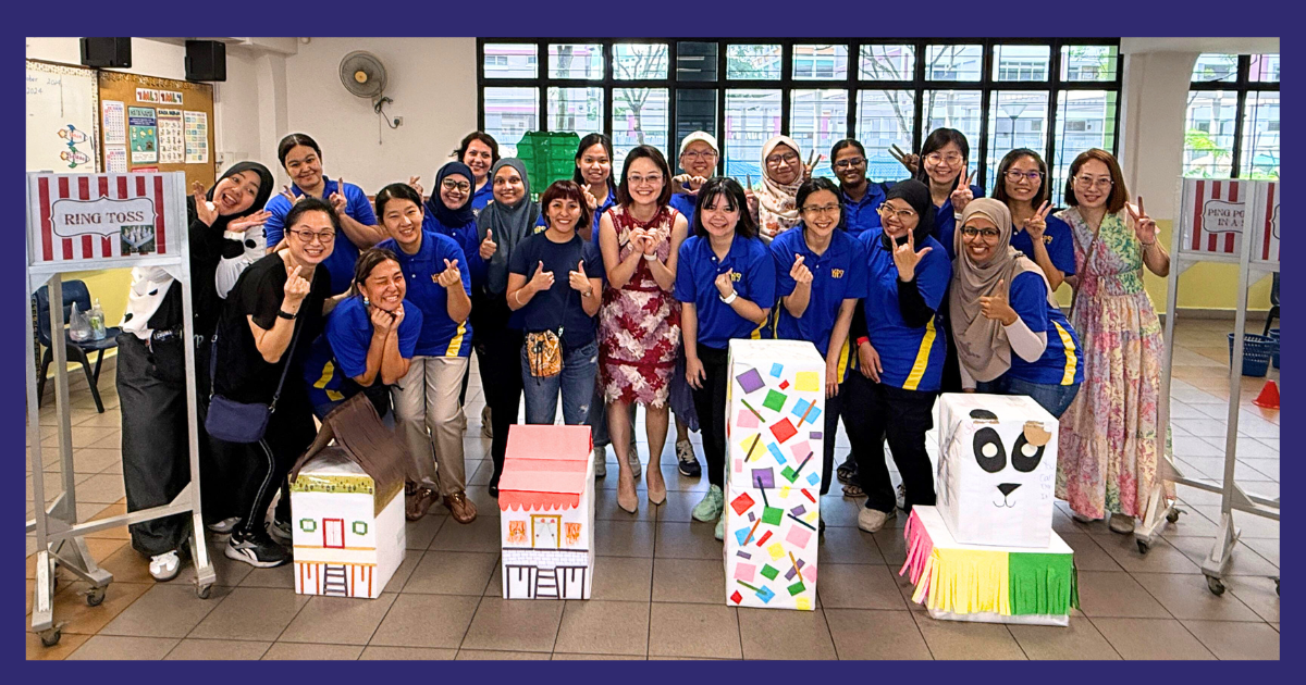 A group of people in blue uniforms pose smiling with colorful decorated cardboard boxes in an indoor hall.