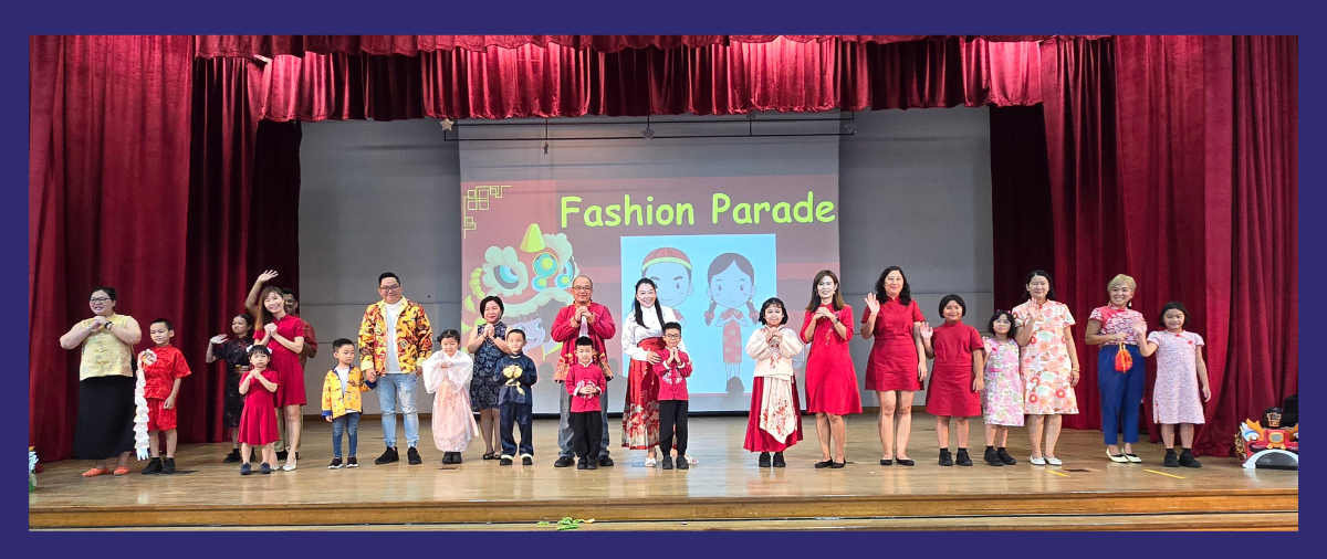 Adults and children in traditional Chinese outfits stand on a stage during a Fashion Parade event with red curtains.