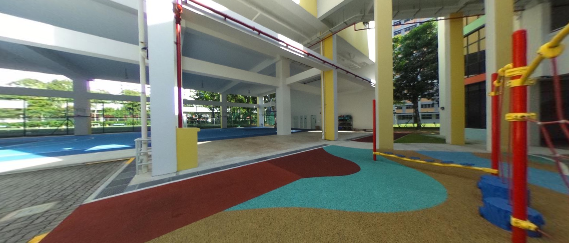Covered school playground with colorful rubber flooring in red, teal, and tan, with yellow and red climbing equipment.