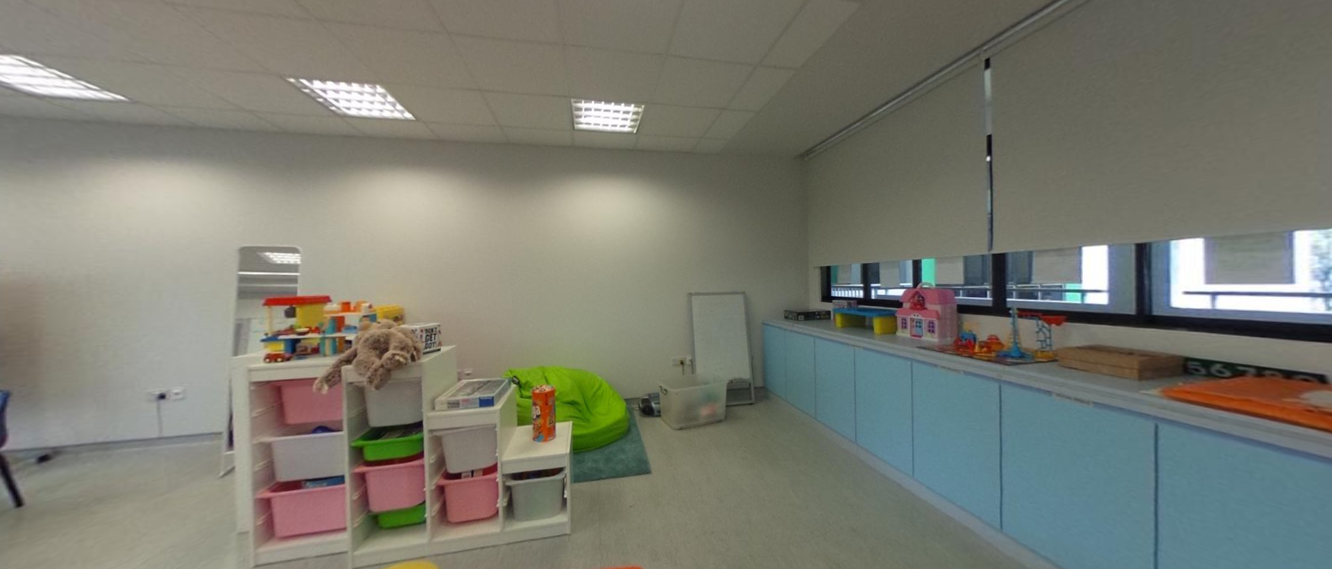 A bright children's playroom with colorful toy shelves, a green bean bag, and toys along a light blue counter.