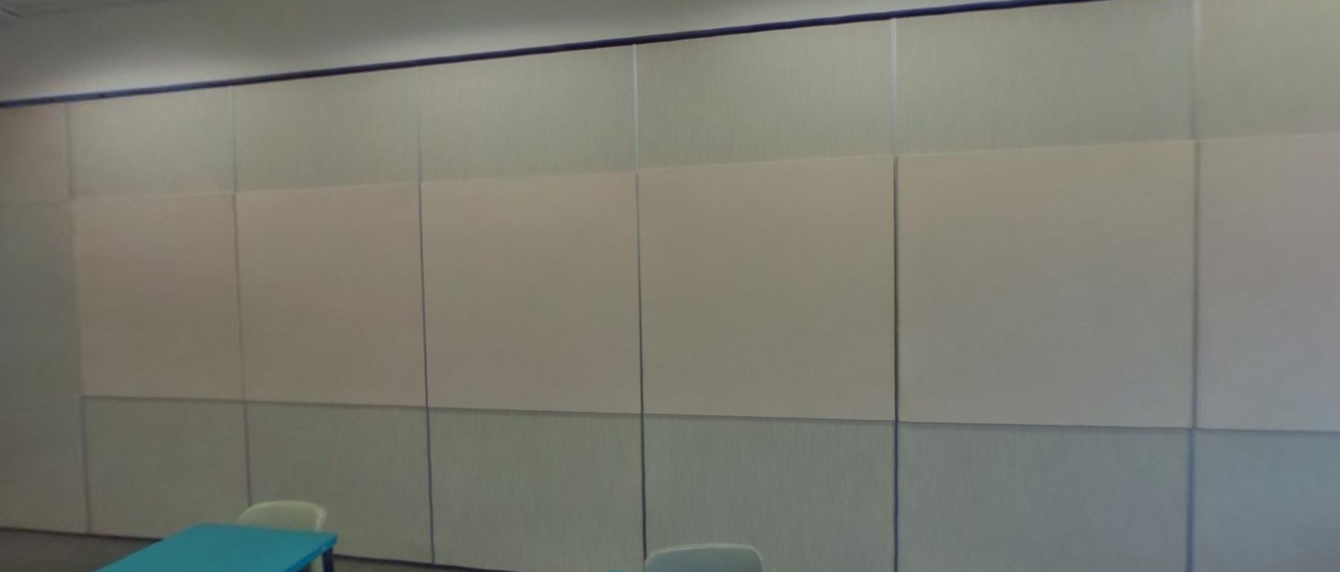 A large beige folding partition wall in a room with a blue table and two chairs visible at the bottom.