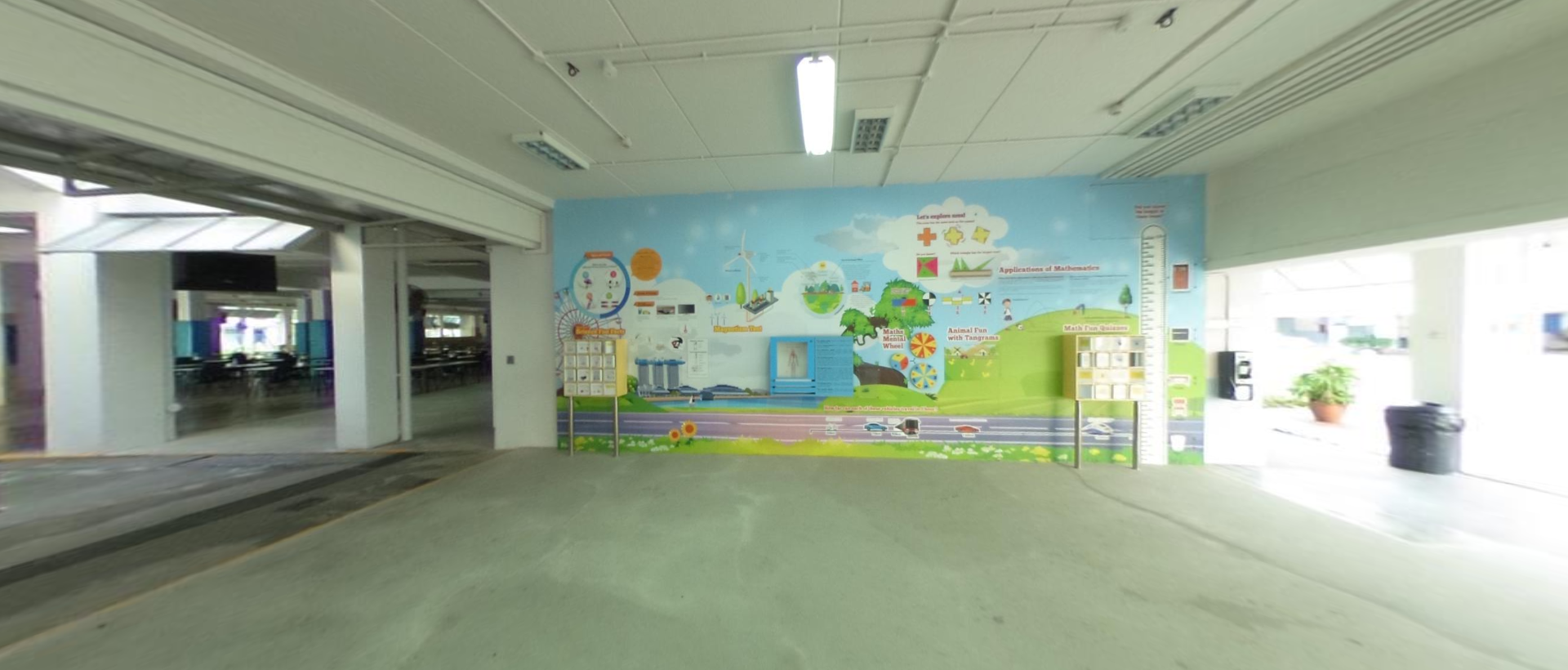A large colorful educational mural about mathematics covers a wall in a covered corridor with concrete floors.