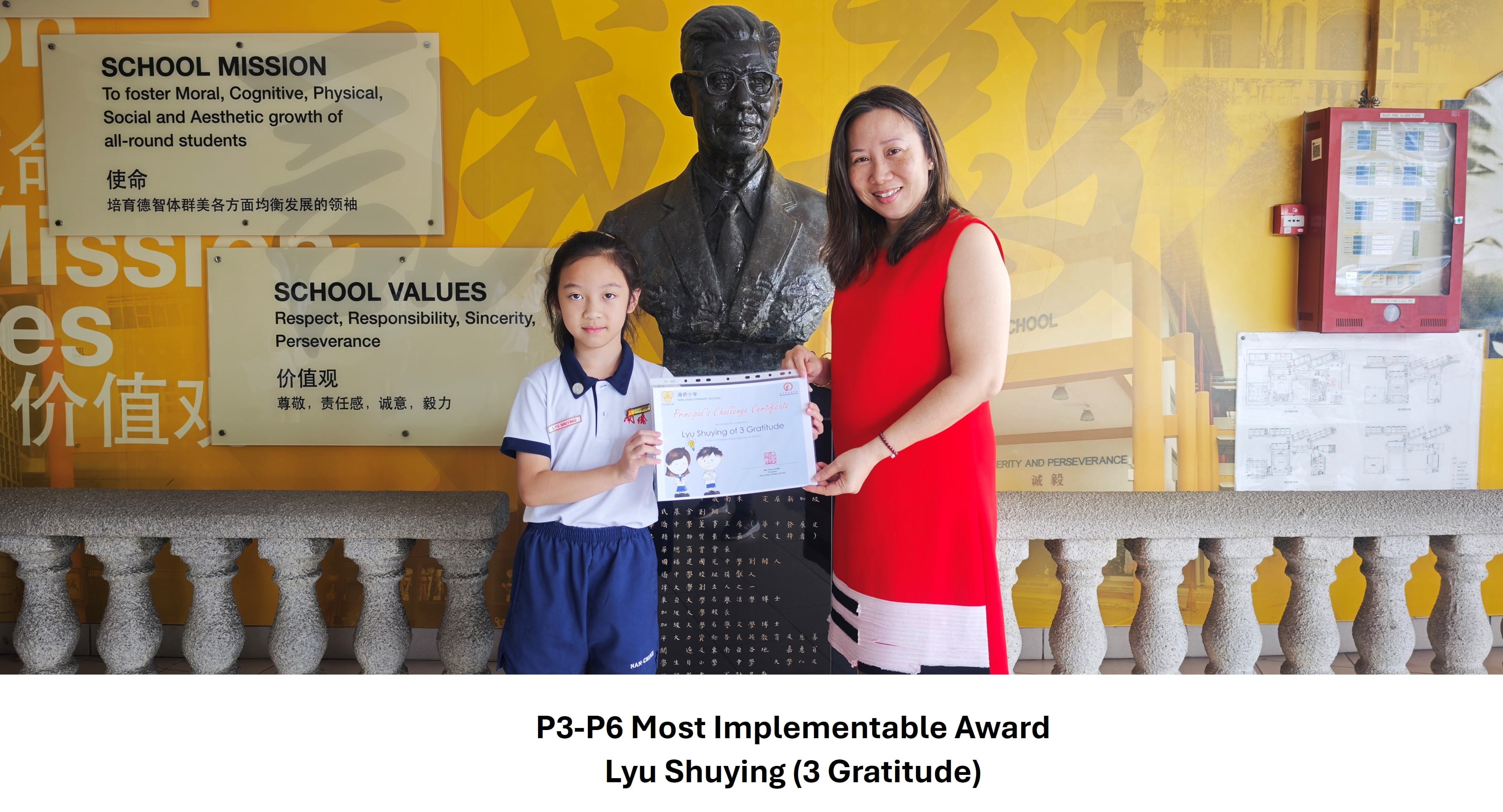 A young girl in school uniform and a woman in red hold a certificate together in front of a bronze bust at school.