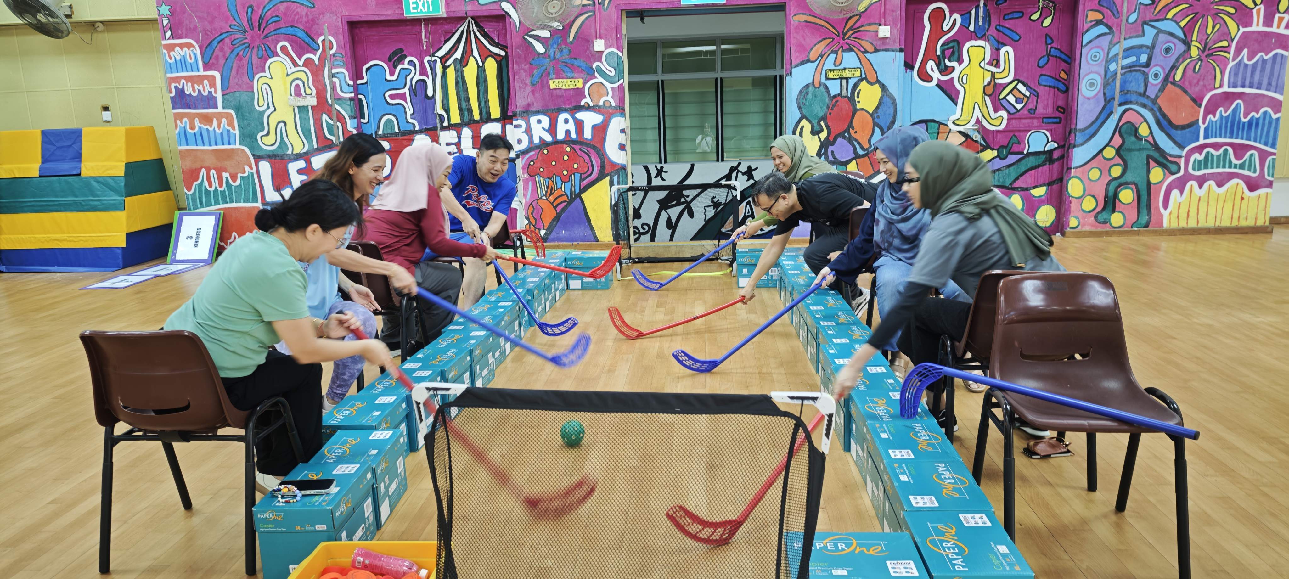NCPS teachers seated on the chair playing a seated floor hockey game.