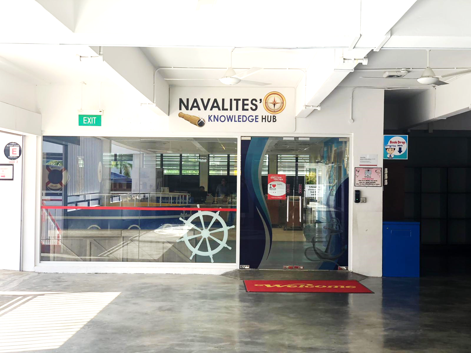 Entrance of Navalites' Knowledge Hub with glass doors, a ship wheel decal, and a red Welcome mat.
