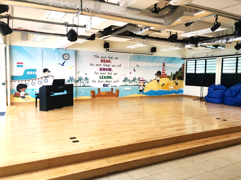 A school stage with a colorful Dr. Seuss reading quote mural, a Casio piano, and stage lighting above.
