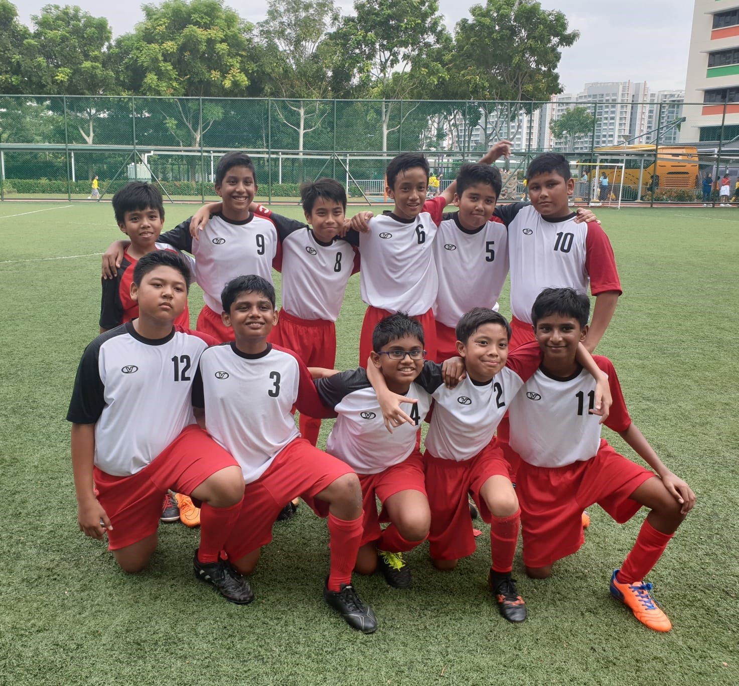 A youth soccer team of eleven boys in white and red uniforms posing together on a green turf field.