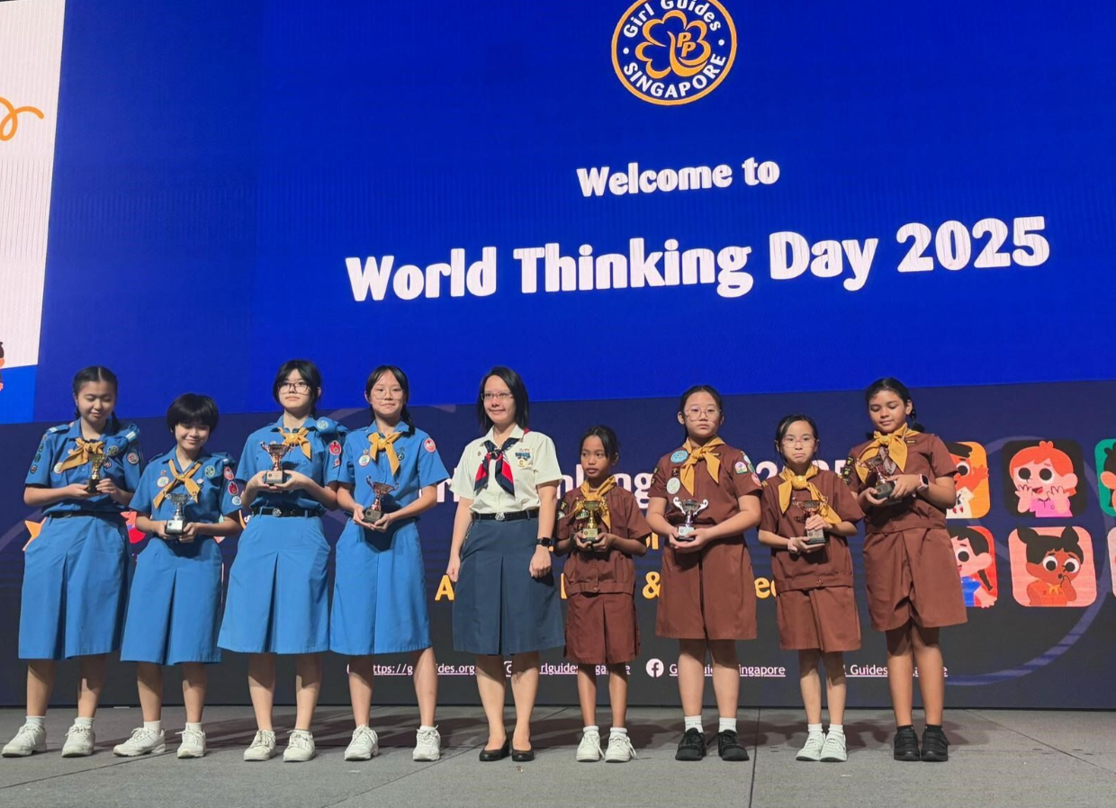 Girls in scout uniforms holding trophies on stage at Girl Guides Singapore World Thinking Day 2025 event.