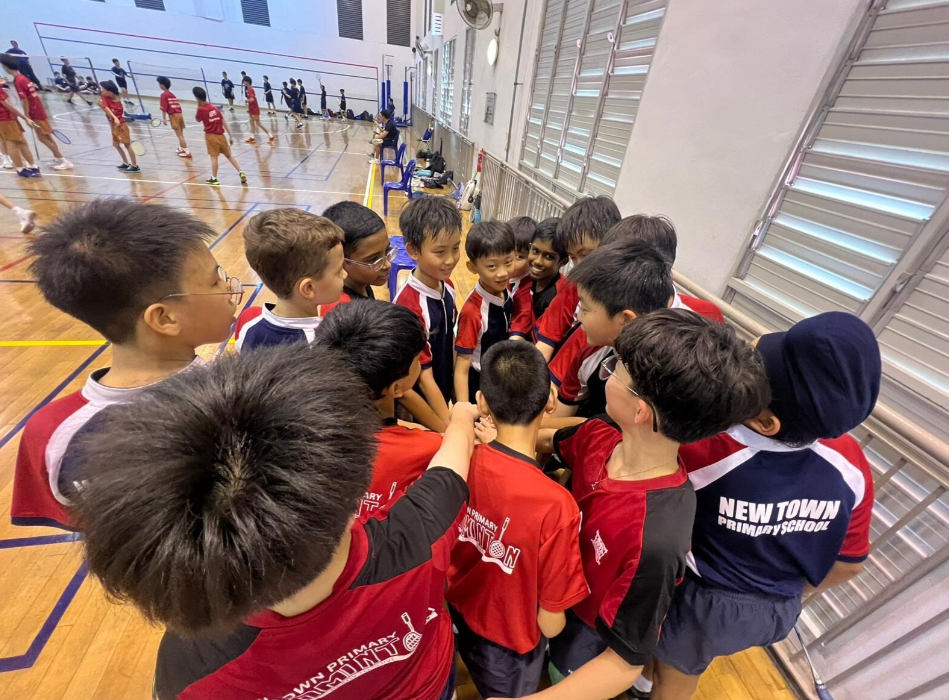 New Town Primary School boys in red uniforms huddle together on an indoor badminton court.
