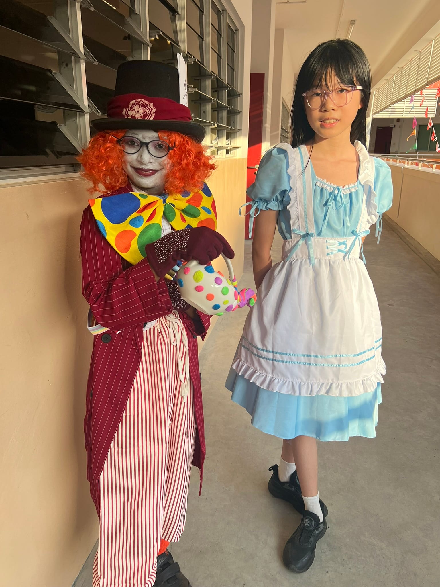 Two people in costumes: one as the Mad Hatter with orange wig and top hat, one as Alice in a blue dress.