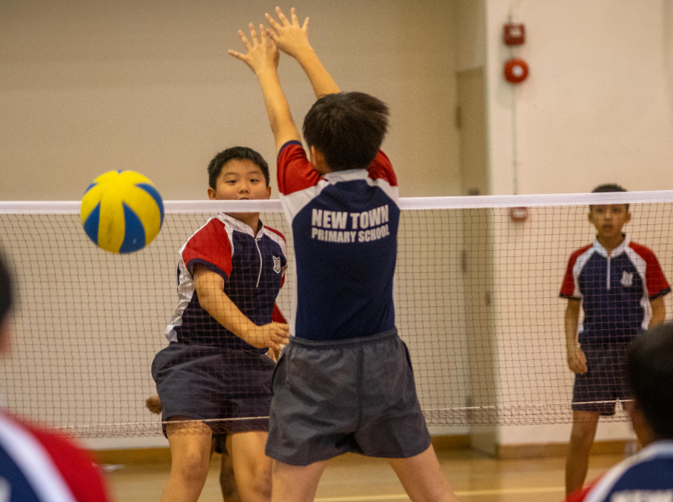 A boy in school uniform striking the ball across the net while playing volleyball