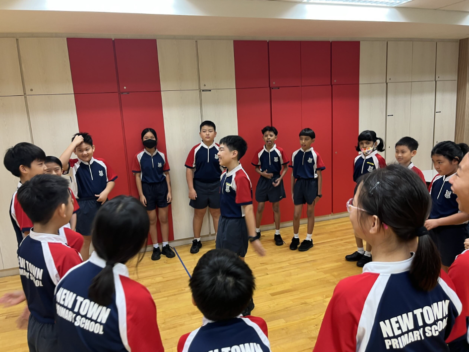 Students in New Town Primary School uniforms stand in a circle on a wooden floor in an indoor hall.