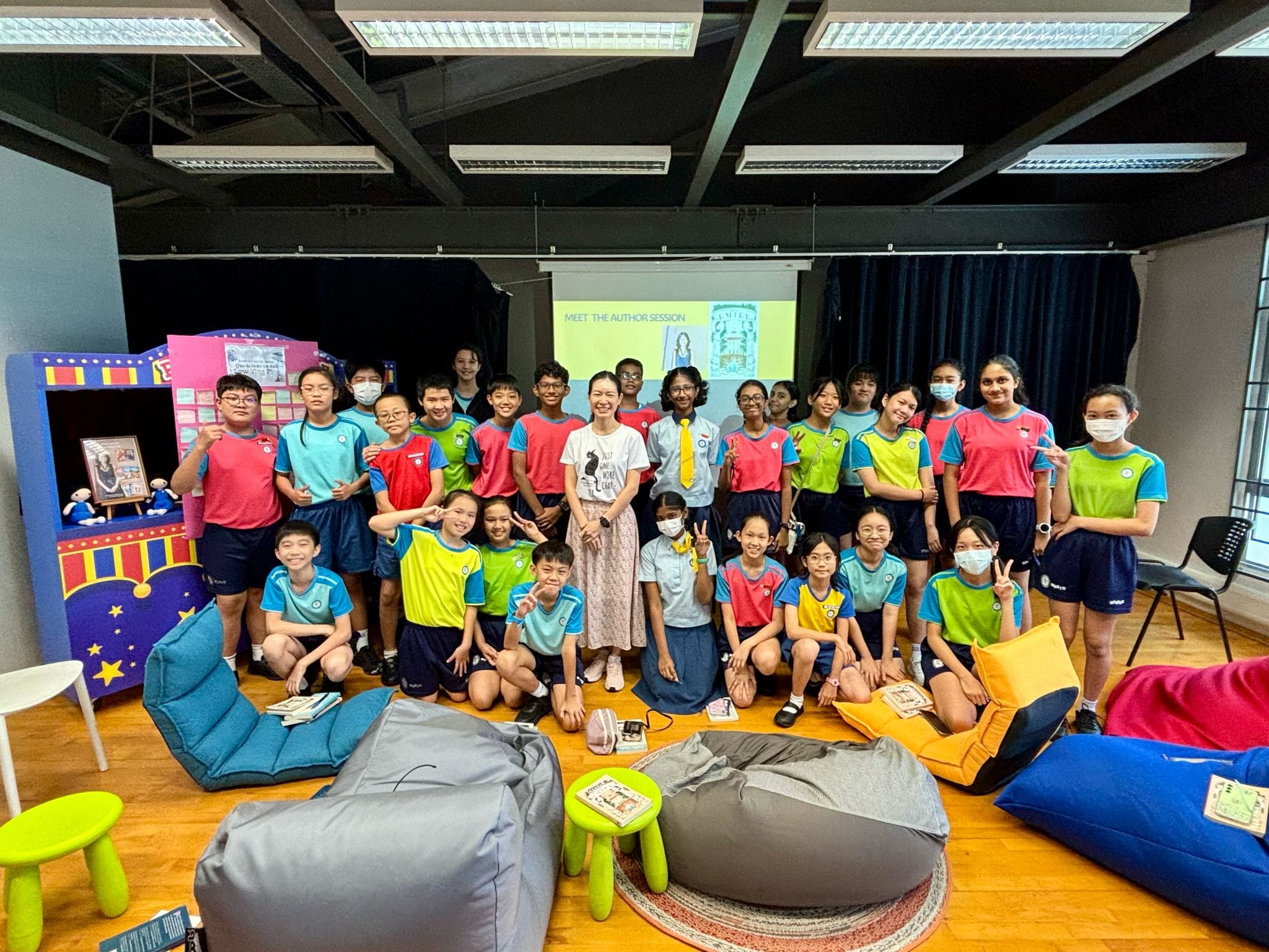 A group of school children in colorful uniforms pose with an adult woman at a Meet the Author Session.