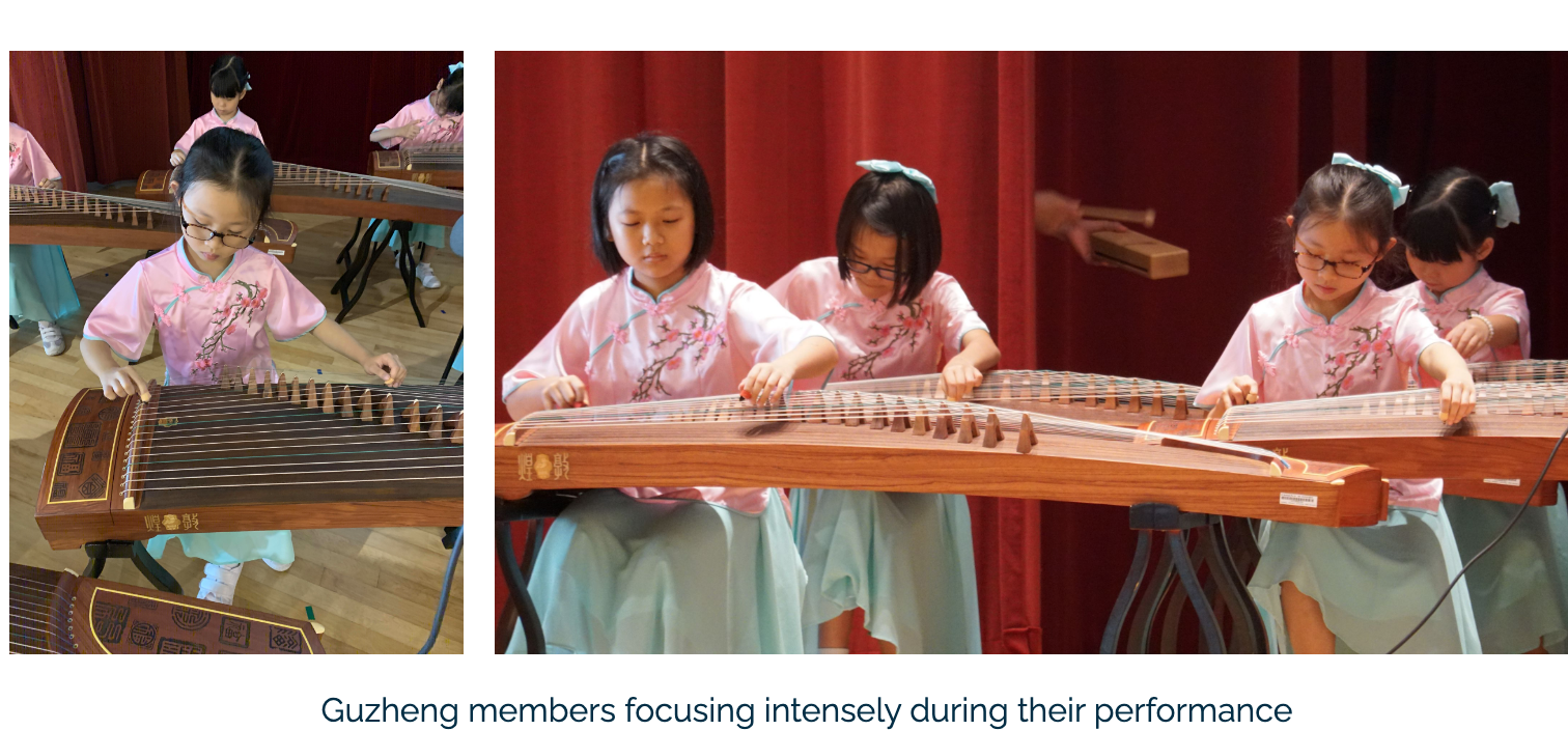 Young girls in pink floral outfits play Guzheng instruments during a stage performance with a red curtain backdrop.
